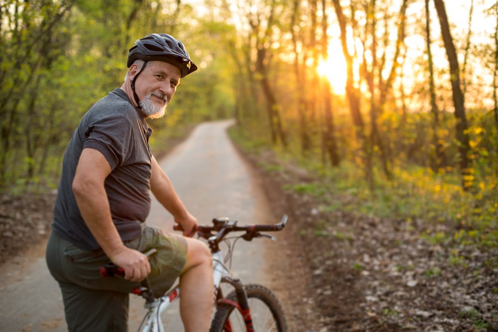 A man pausing on a forest bike trail at sunset.